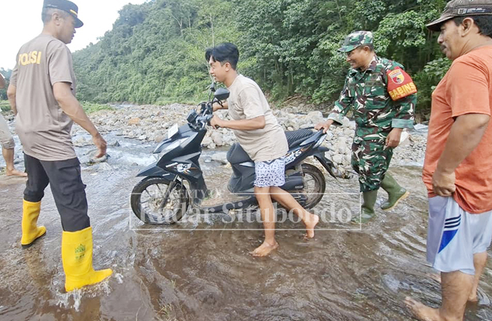 LEWATI SUNGAI: Seorang warga meminta bantuan untuk menyeberang sungai karena jembatan putus akibat banjir, Minggu (25/1).