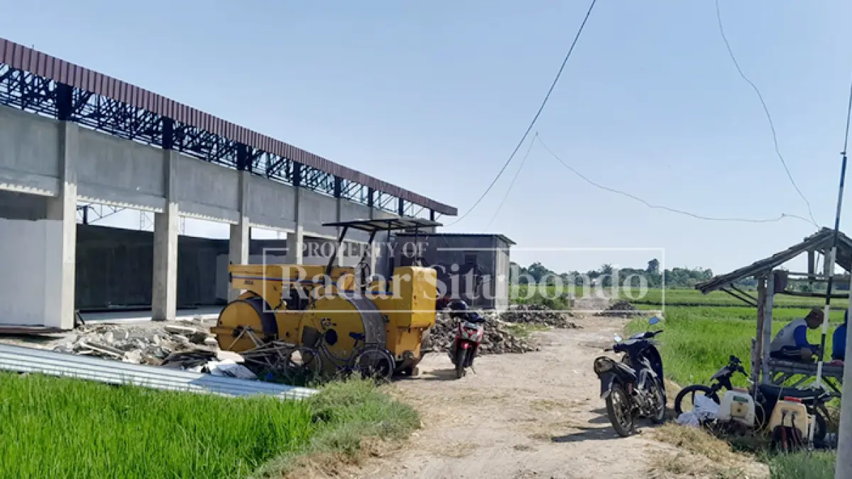 TAK ADA PEKERJA: Salah satu pencari rumput melintas di depan pembanguan gedung KDMP Desa Tenggir, Kecamatan Panji, Selasa (2/6). (HUMAIDI/JPRS)
