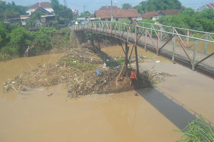 BERJIBAKU: Warga melakukan pembersihan sangkrah yang nyangkut tiang jembatan Desa Karobelah, Kecamatan Mojoagung, Selasa (9/1).