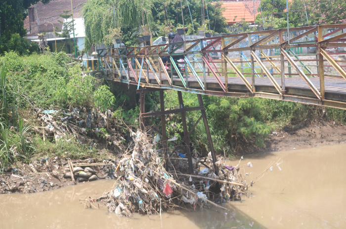 MENUMPUK: Sampah plastik dan ranting pohon bambu yang terbawa aliran Kali Gunting tersangkut tiang jembatan di Desa/Kecamatan Sumobito.