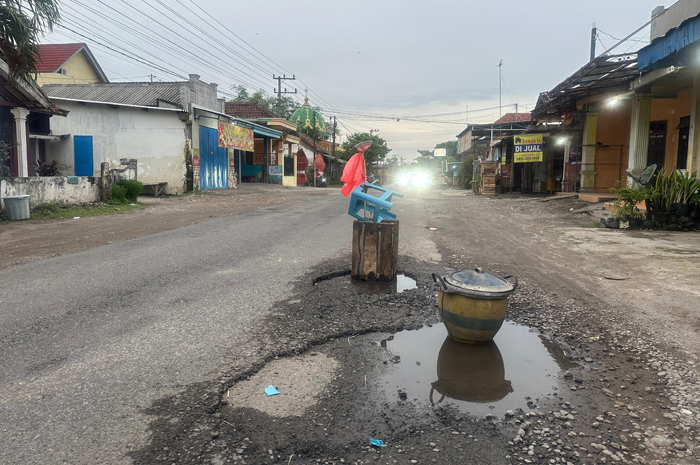 BAHAYA: Lubang jalan di Desa Menganto, Kecamatan Jogoroto, Jombang makin dalam ditandai peti dan kursi bekas.
