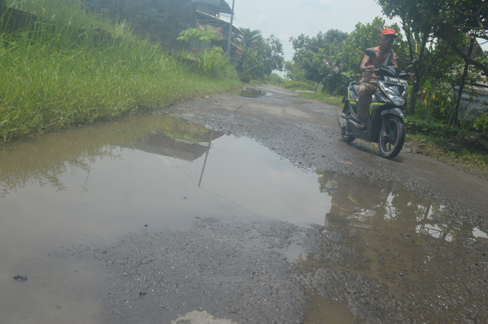 KUBANGAN AIR: Pengendara sepeda motor melewati jalan kabupaten di Desa Dukuhklopo, Kecamatan Peterongan, Jombang yang rusak.