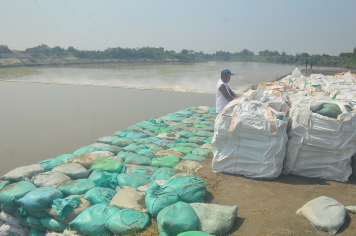 DIPASANG: Salah seorang penjaga Dam Karet Jatimlerek di sisi Desa Sudimoro, Kecamatan Megaluh, Jombang, berada di antara sandbag dan jumbobag yang baru saja dipasang dekat pintu enam yang jebol.