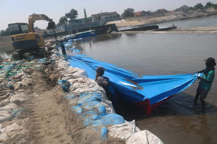 SEGERA TUNTAS: Pekerja tengah memasang jumbo bag dan terpal untuk pembangunan kisdam di pintu enam Dam Karet Jatimlerek Jombang yang jebol.