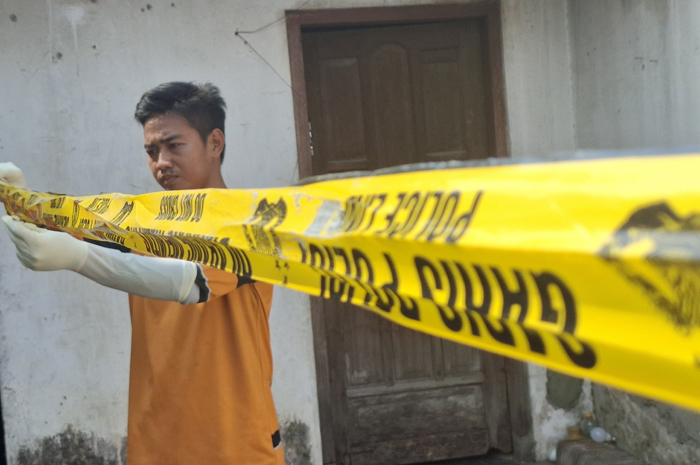 GARIS POLISI: Petugas memasang garis polisi di lokasi penemuan pria yang tewas membusuk di rumah kontrakan Dusun Karangtengah, Desa Johowinong, Kecamatan Mojoagung, Jombang, Rabu (25/6) pagi