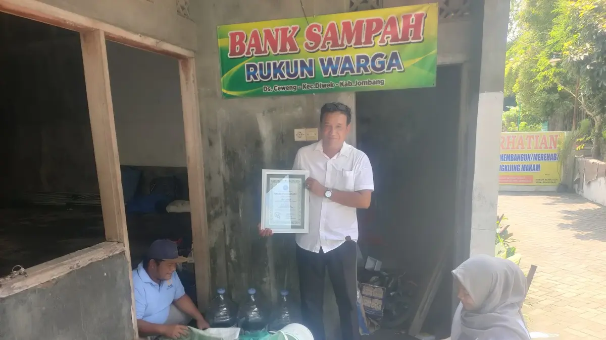 PEDULI LINGKUNGAN: Kepala Desa Ceweng Imam Subata (berdiri) menunjukkan piagam penghargaan yang diraih Bank Sampah Rukun Warga Ceweng, Diwek, Jombang. (Dwi Aris/Radar Jombang)