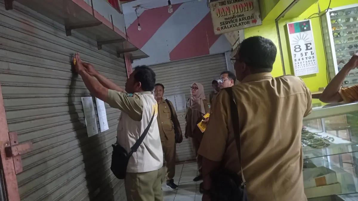 DISEGEL: Petugas Disdagrin Jombang memasang stiker segel pada kios PCN Jombang, Senin (25/8). (Ainul Hafidz/Radar Jombang)