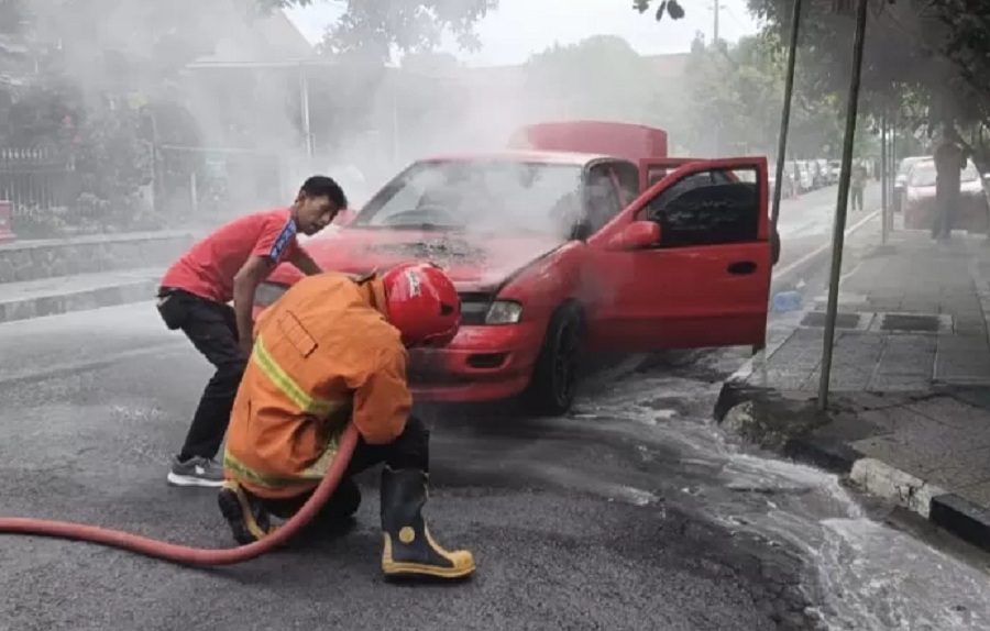 Petugas damkar melakukan pemadaman dan pendinginan pada mobil yang terbakar.