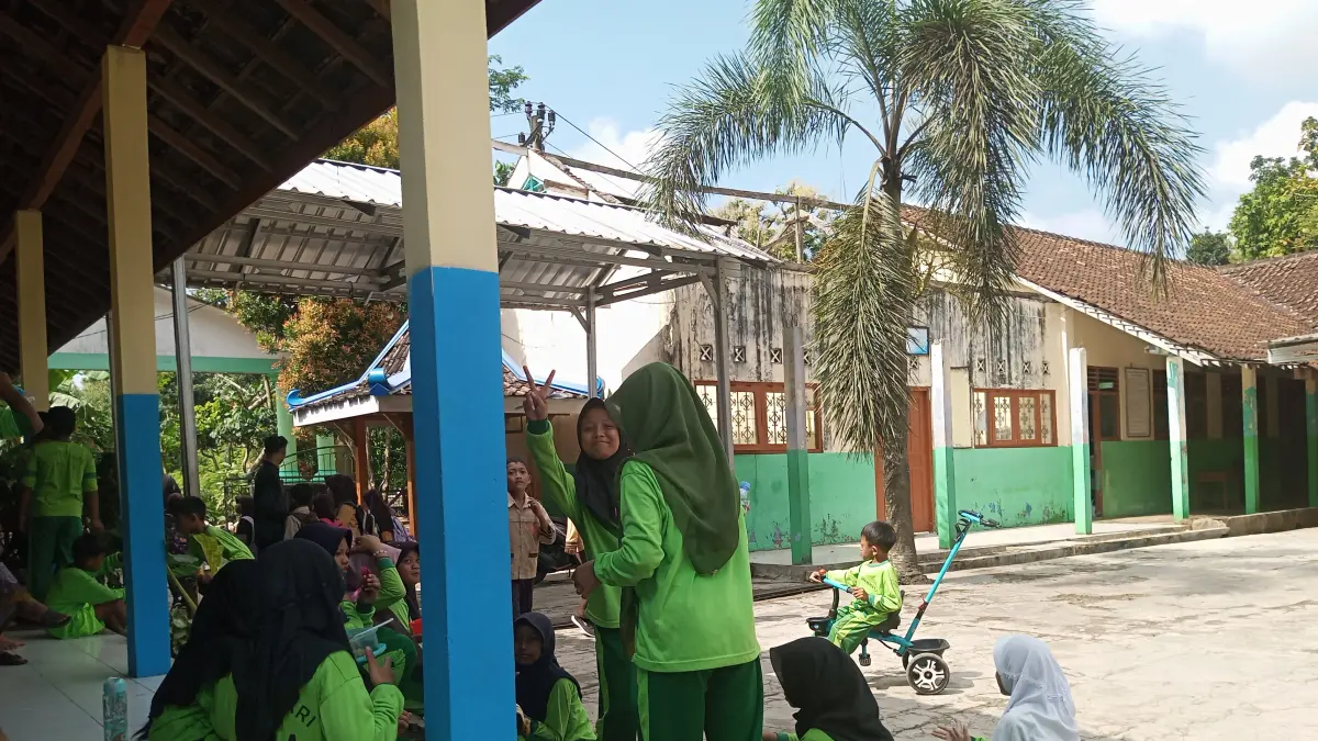 Siswa SD Kepek 1 Saptosari sedang menyantap menu MBG tepat di depan gedung perpustakaan yang rusak parah.
