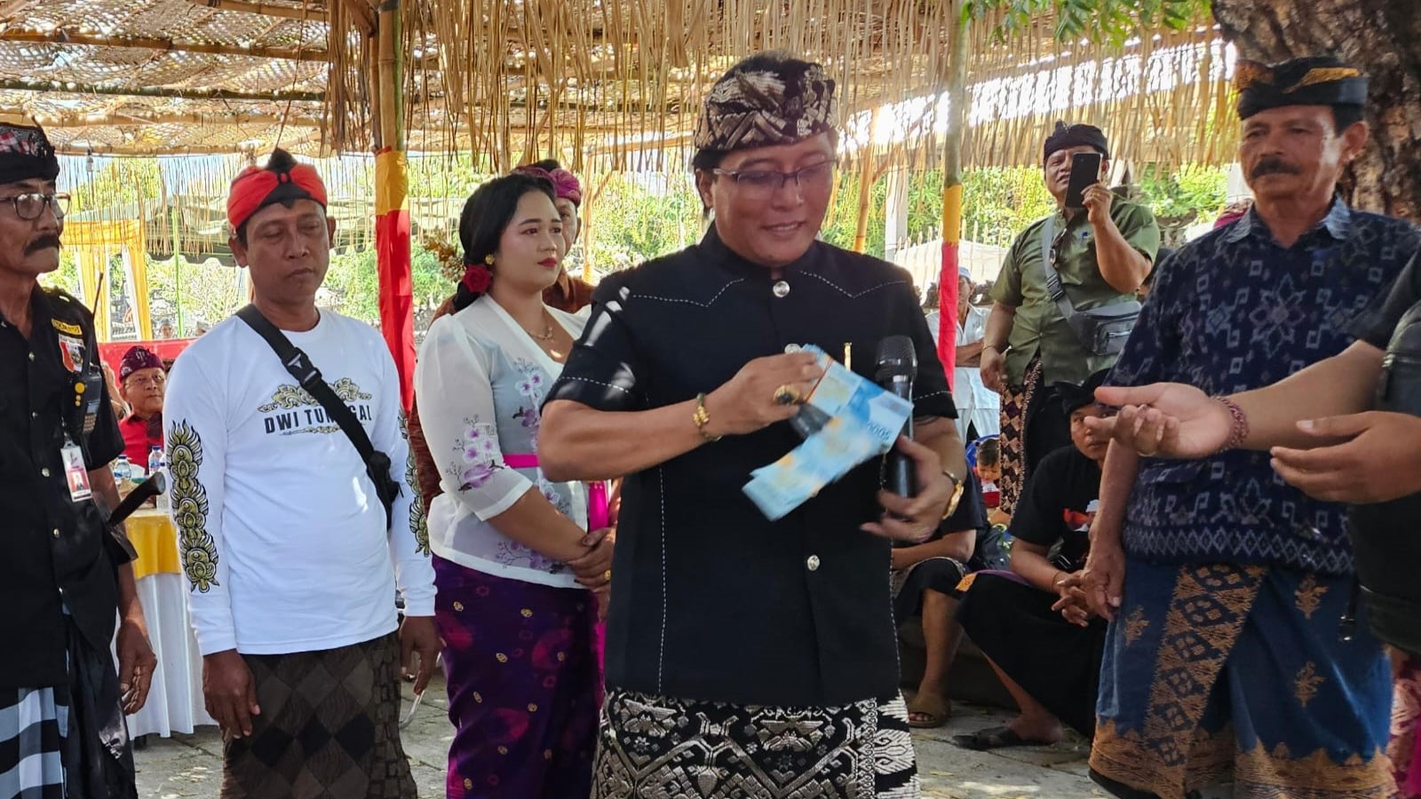 SAMPAI JATUH: Bupati Badung, Nyoman Giri Prasta saat hendak menyerahkan punia pada acara Ngaben Massal di Desa Adat Tinga-Tinga. Saking banyaknya, uang yang dibawa sampai jatuh.