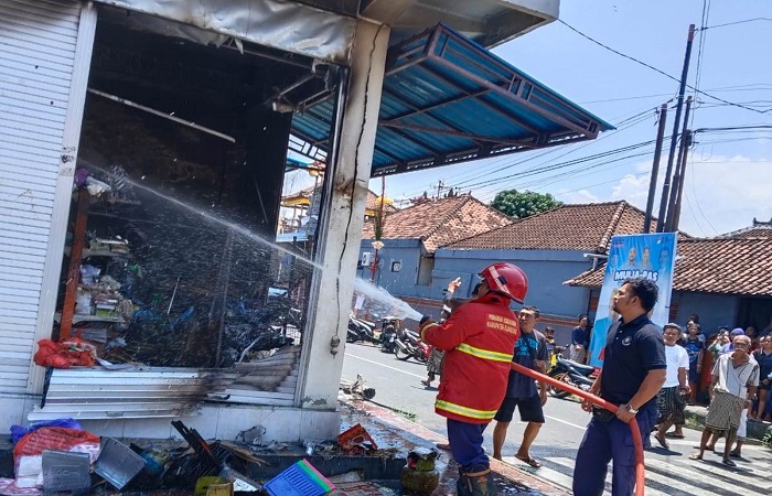 Petugas Damkar berupaya memadamkan api yang membakar kios sembako.
