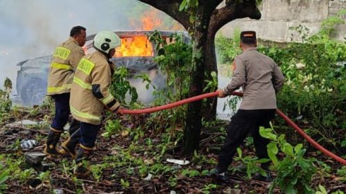 TERBAKAR: Polisi dan pemadam kebakaran berusaha memadamkan api yang membakar sebuah mobil. Mobil itu mengangkut belasan jerigen bekas.
