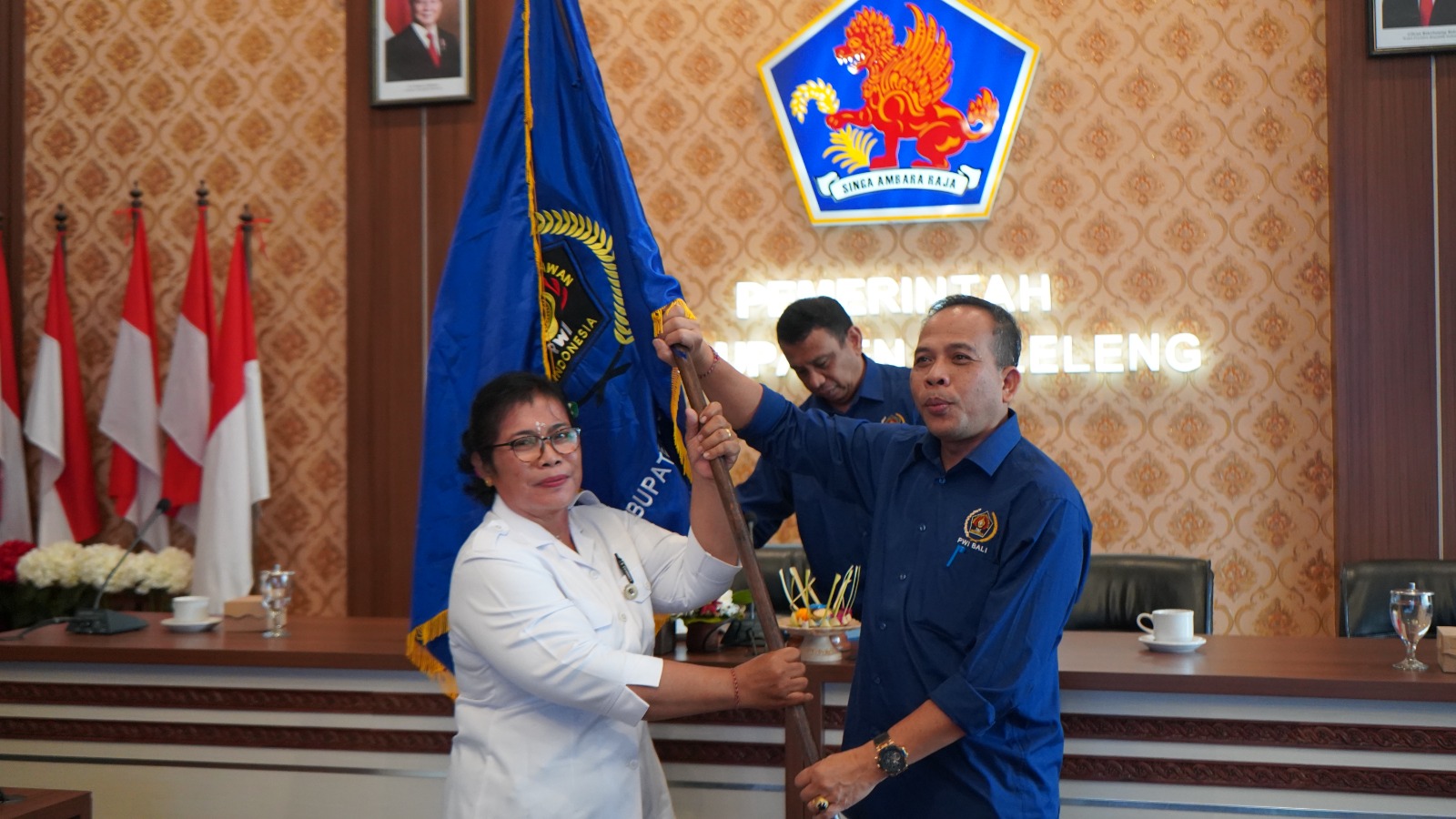 AKLAMASI: Ketua PWI Bali, Wayan Dira Arsana (kanan) mengerahkan bendera PWI kepada Ketua PWI Buleleng, Made Winingsih (kiri).