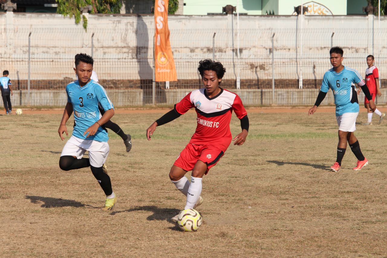 JAGA BOLA: Pemain Temukus FC (baju merah) mengawal bola dari jangkauan pemain Putra Harapan Kaliasem (biru) dalam kompetisi Liga 3 Askab PSSI Buleleng.
