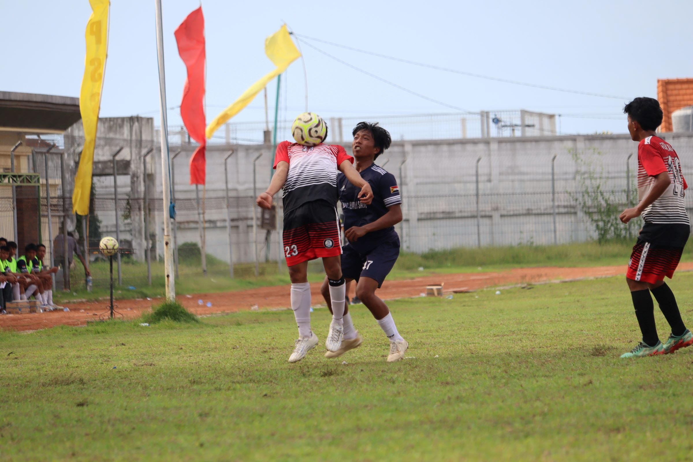 WAJAH BOLA: Pemain Forkal Kalibukbuk (merah) berusaha mengendalikan bola dari pemain Satria Muda Pengulon (biru) dalam pertandingan di Stadion Mayor Metra Singaraja, Minggu (30/11/2025).
