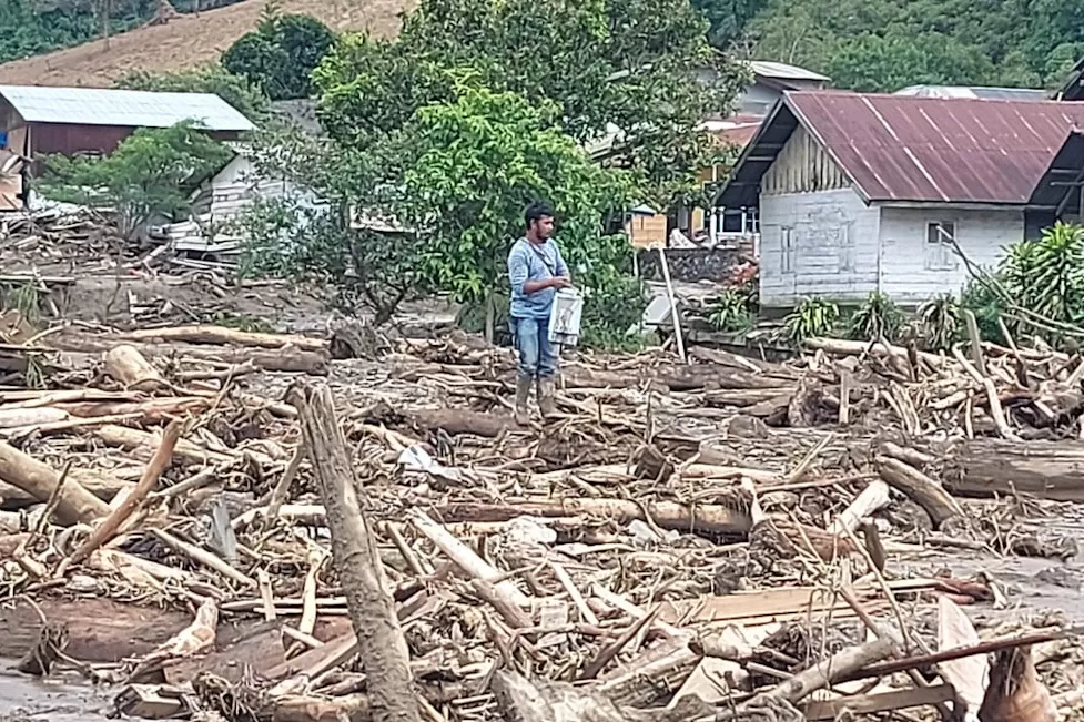 Warga Takengon, Aceh Tengah, berdiri di antara kayu-kayu yang terbawa banjir dan longsor.