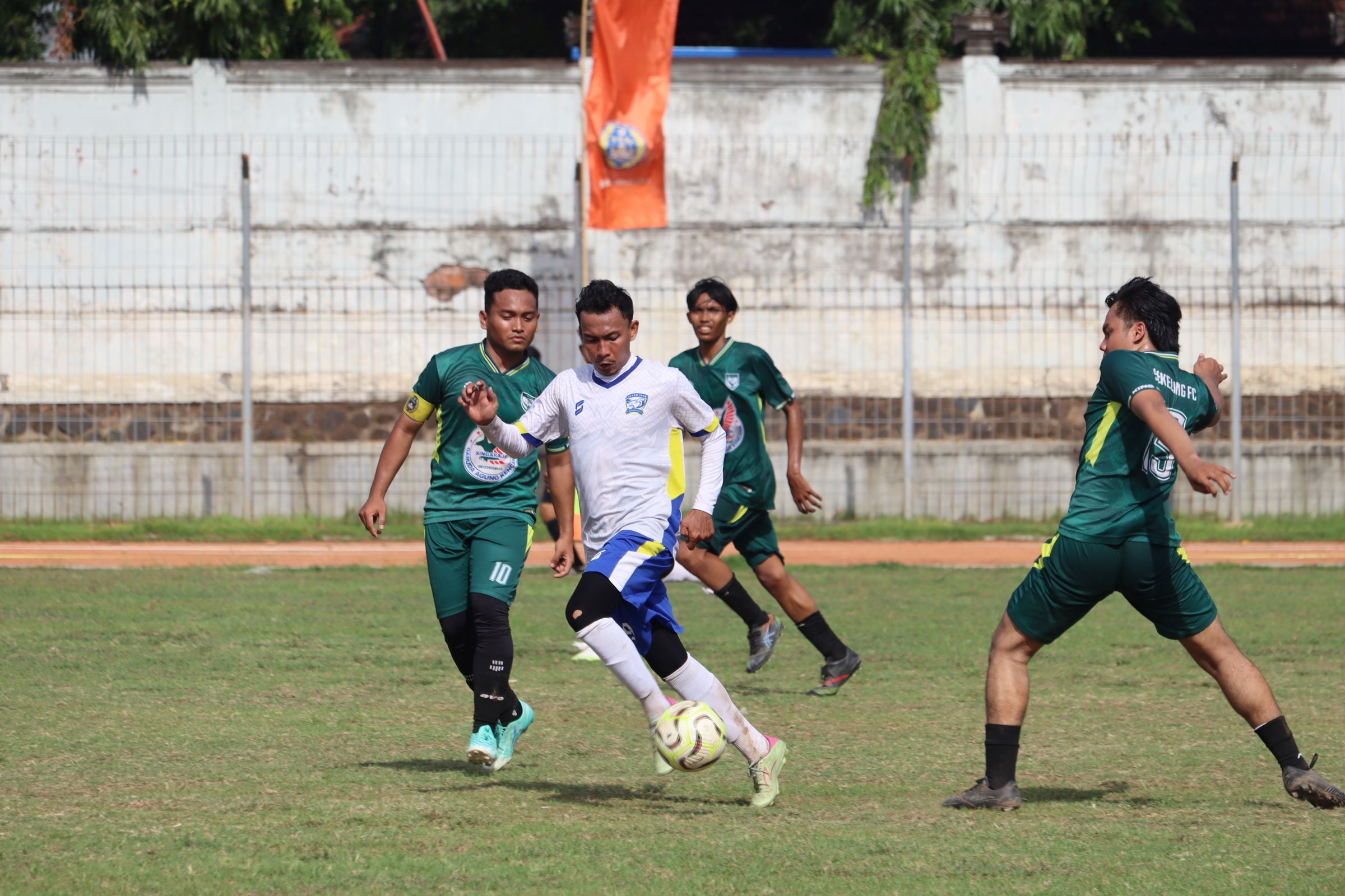 DOMINAN: Pemain Intan Jaya Celukan Bawang (baju putih) lepas dari kawalan pemain Sekeling FC Penyabangan (hijau) dalam pertandingan di Stadion Mayor Metra Singaraja, Senin (8/12/2025).
