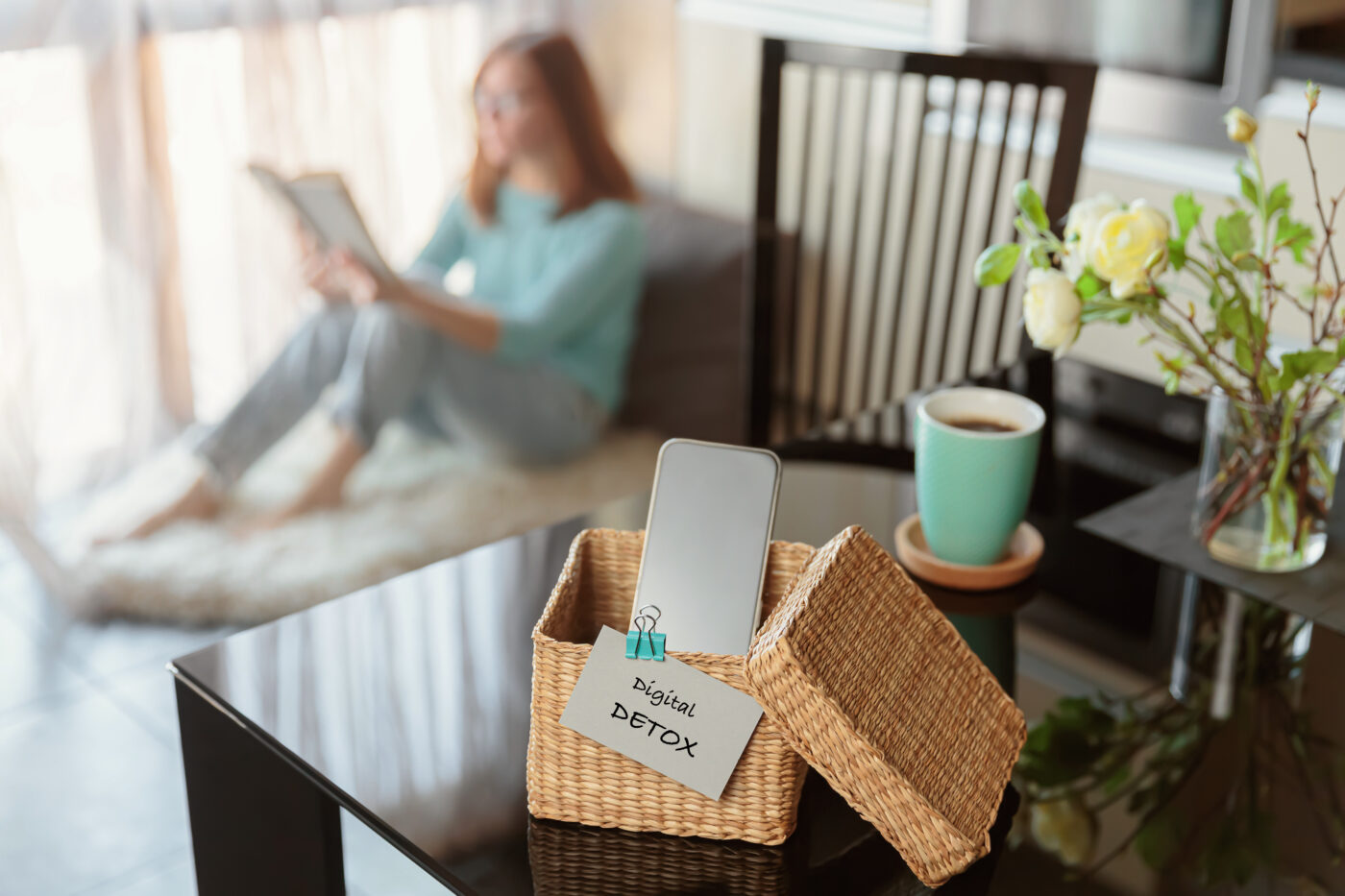 Sebuah smartphone disimpan di kotak anyaman bertuliskan "digital detox" di atas meja. Di kejauhan, seorang wanita tampak asyik membaca buku. Saatnya rehat sejenak dari gawai. Detoks digital dan mental