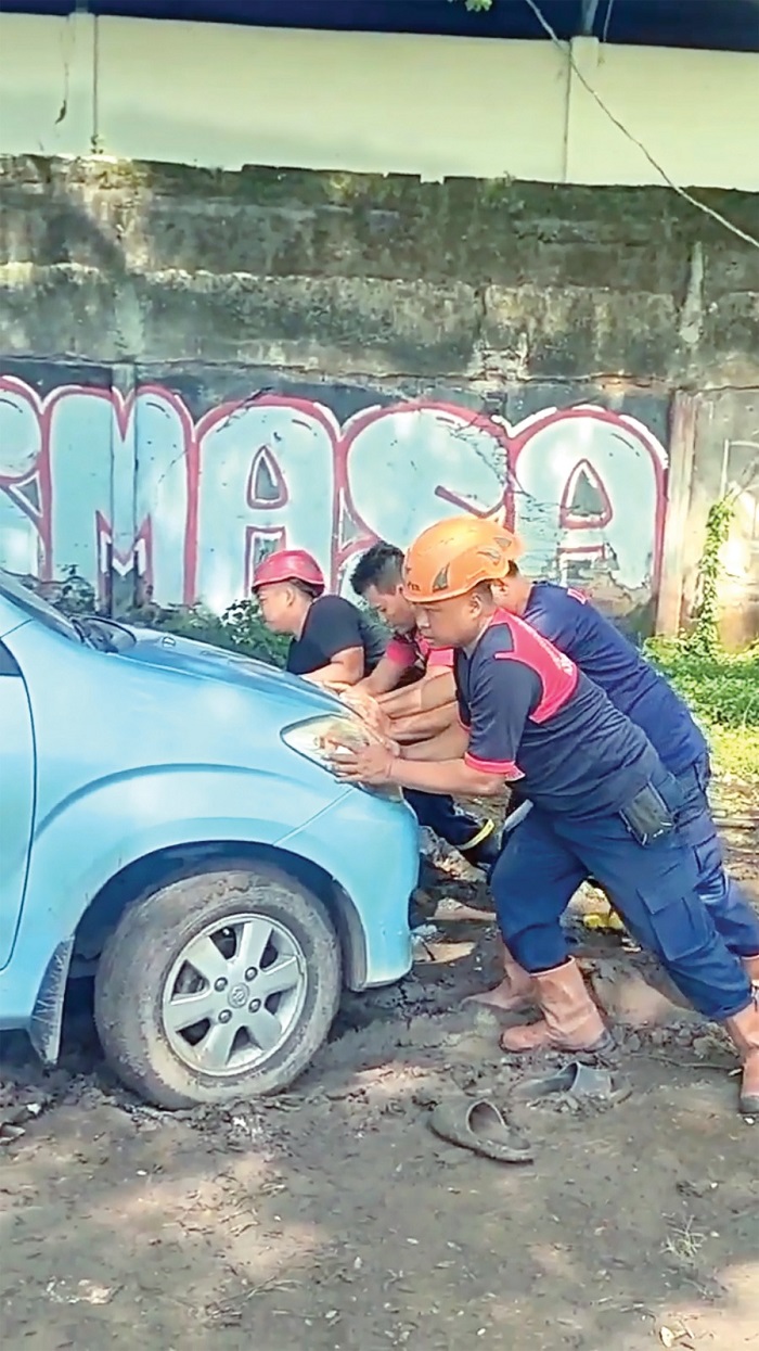 Petugas damkarmat Nganjuk mendorong mobil yang terjebak lumpur di Lapangana Cangkringan