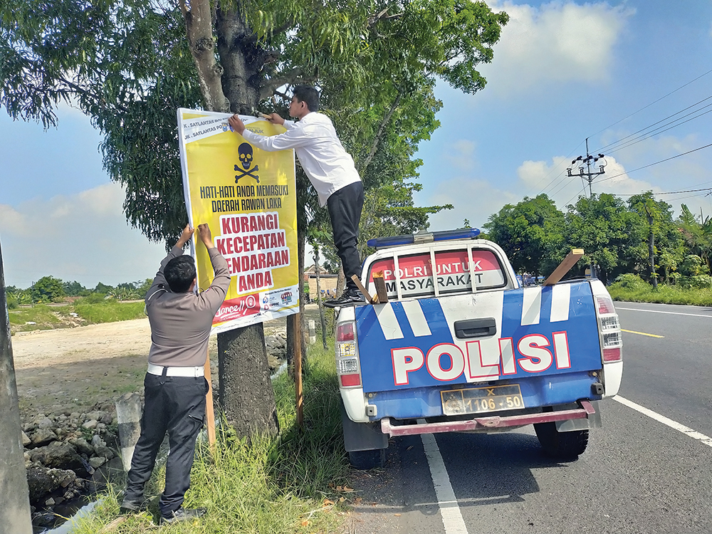 RAWAN LAKA: Petugas Satlantas Polres Nganjuk memasang banner imbauan karena angka kecelakaan tinggi.