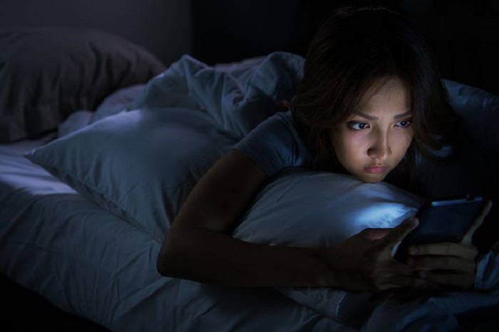 Ilustrasi seorang perempuan begadang sambil bermain handphone.