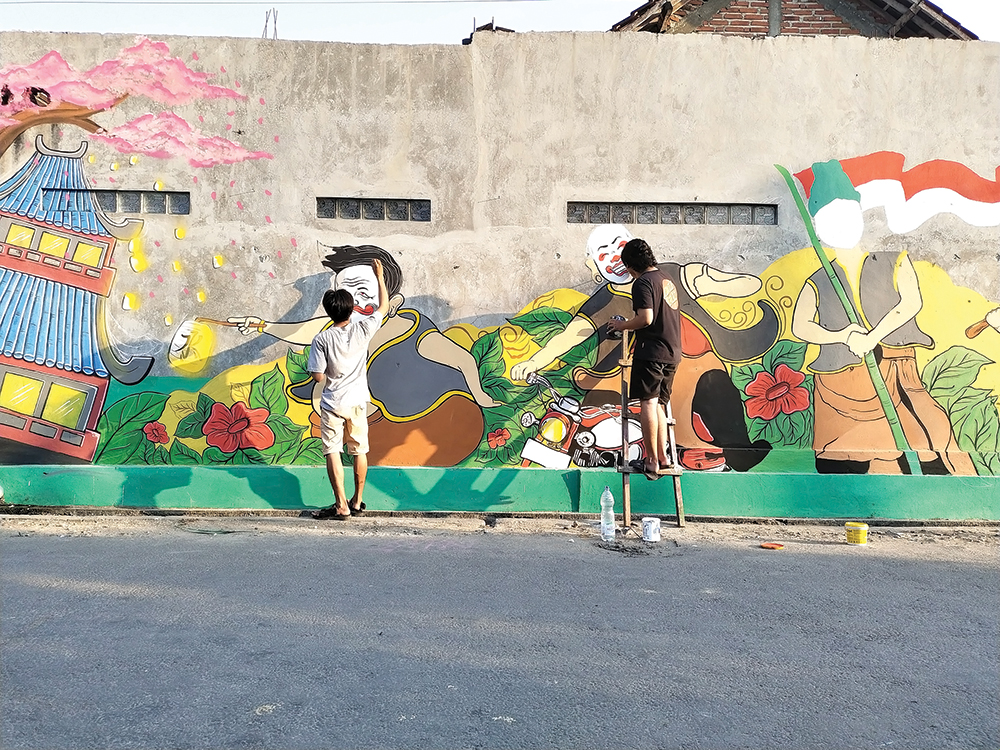 PERCANTIK KOTA: Brian Sena Indrajati (kiri) melukis di tembok jalan Kota Angin. Muralis andalan Kabupaten Nganjuk ini membuat tembok kosong dan berlumut menjadi indah.