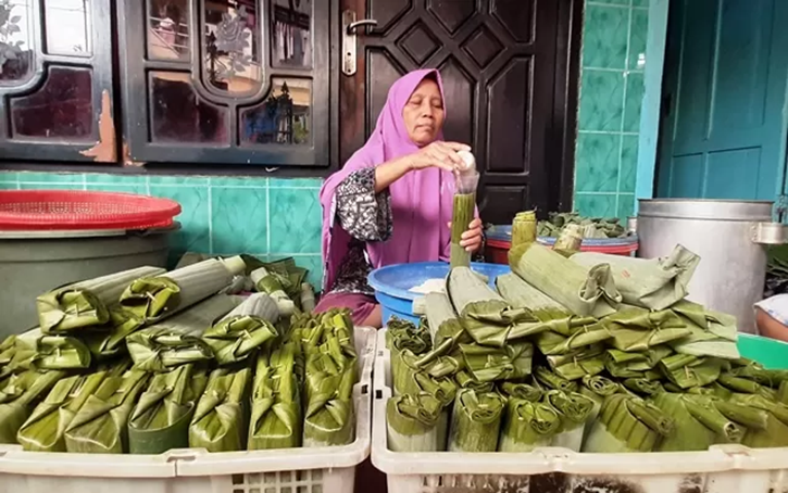 TELATEN: Salah satu pembuat lontong di Kampung Lontong, Sutri, 63, sedang memasukkan beras ke dalam daun pisang