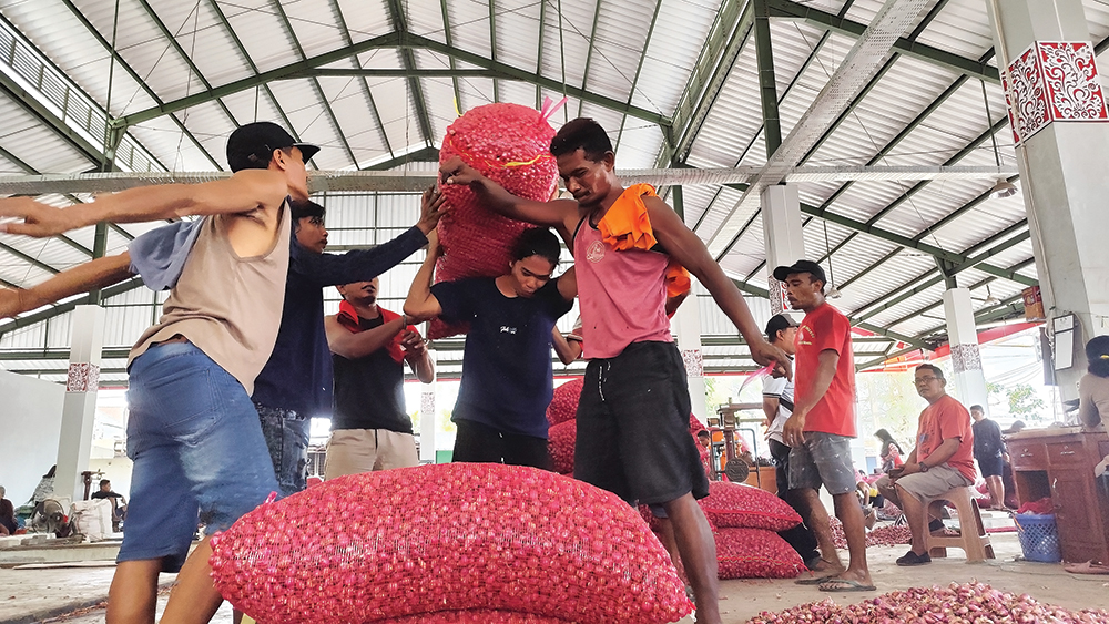 NAIK LAGI: Pedagang di Pasar Bawang Merah Sukomoro mengangkat brambang untuk ditimbang kemarin. Harga bawang merah lokal menembus Rp 44 ribu per kilogram.