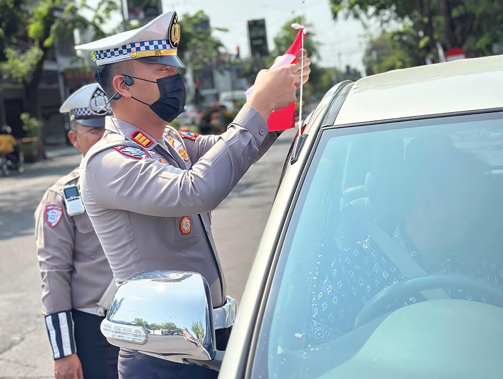 SEMANGAT KEMERDEKAAN: Kasatlantas Polres Nganjuk AKP Ivan Danara Oktavian membagikan bendera pada pengguna jalan yang melintas di Kota Angin.