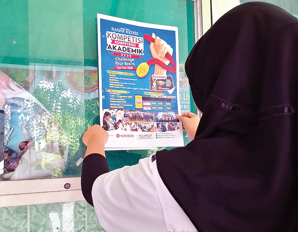 JADI TRY OUT TKA: Siswi memasang poster Kompetisi Kompetensi Akademik JP Radar Kediri di SDN 2 Ploso.