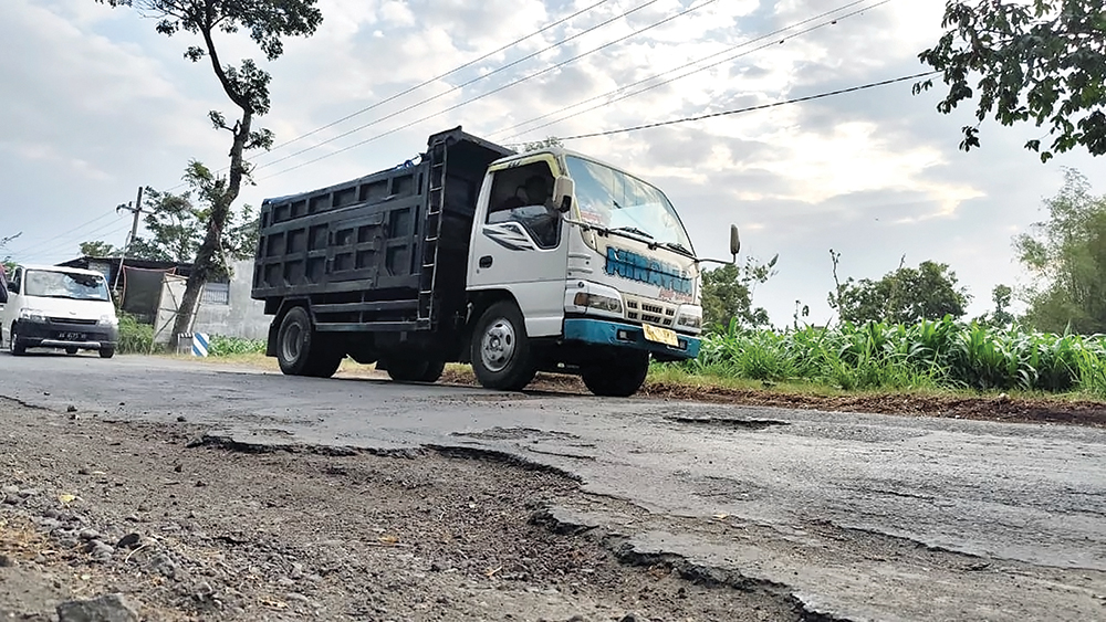 JALAN RUSAK: Truk pasir melintas di Jalan Desa Godean, Loceret yang banyak lubang dan aspalnya mengelupas.