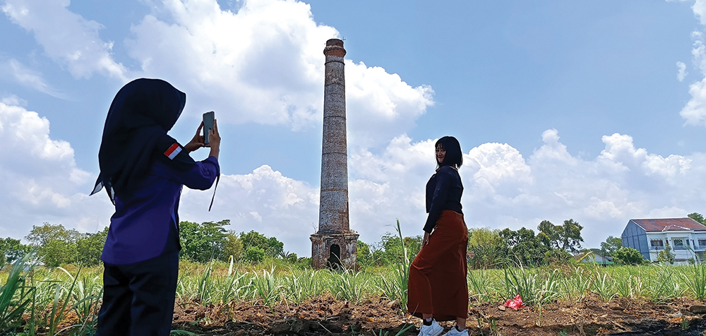 JADI SPOT FOTO: Siswi SMK di Kabupaten Nganjuk foto dengan background stum atau cerobong asap peninggalan Belanda di Desa Jatirejo, Kecamatan Loceret.