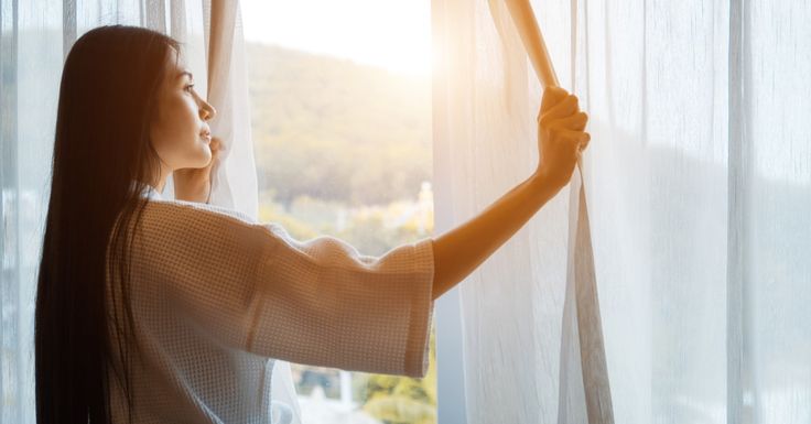 Seorang wanita membuka gorden di pagi hari
