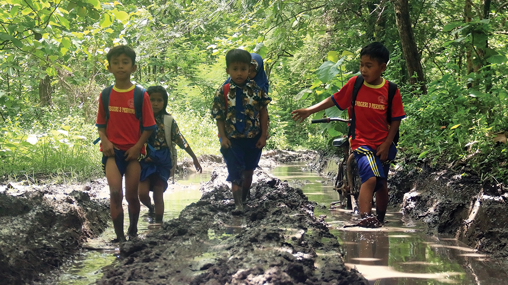 BLETOK: Siswa SDN 3 Perning menuntun sepeda karena jalan berlumpur.