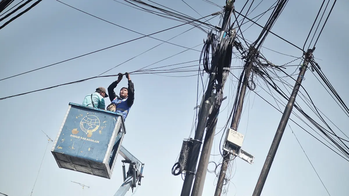 BERGELANTUNGAN: Petugas gabungan Pemkab Nganjuk mengikat kabel wifi ilegal yang bergelantungan di Jalan Raya Nganjuk kemarin. Puluhan wifi ilegal masih marak beroperasi di Kabupaten Nganjuk. (karen wibi/jprk)