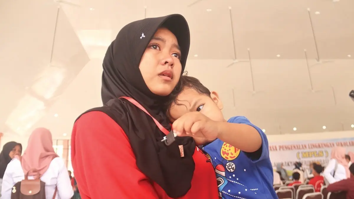 BERSEDIH: Putri Aprilia menggendong adiknya sambil meneteskan air mata kemarin. Siswa Sekolah Rakyat Nganjuk harus masuk asrama di hari pertama masa pengenalan lingkungan sekolah (MPS). (karen wibi/jprk)  