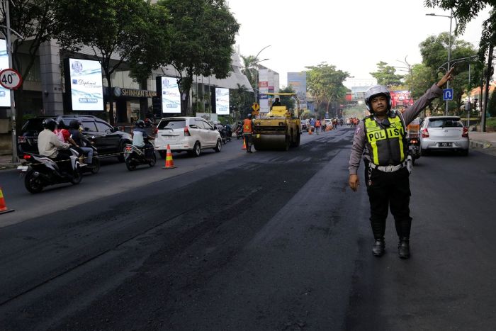 DIASPAL LAGI: Seorang polisi mengatur lalu lintas di sebuah jalan di Kota Surabaya yang sedang dalam proses perbaikan.