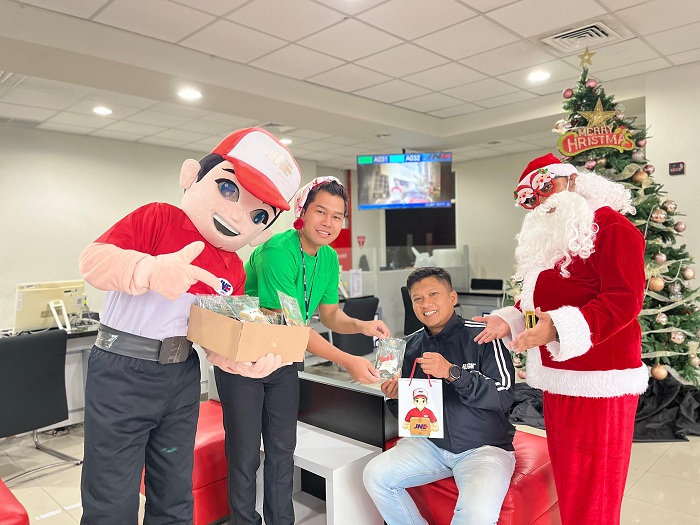 BAHAGIA: Petugas sales counter JNE Surabaya membagikan bingkisan Natal berupa cokelat dan merchandise.