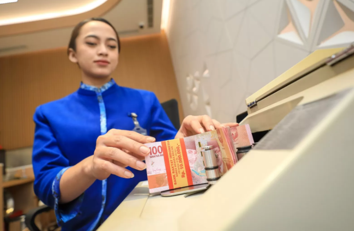 HITUNG: Salah satu teller bank menghitung jumlah rupiah dengan mesin penghitung uang.
