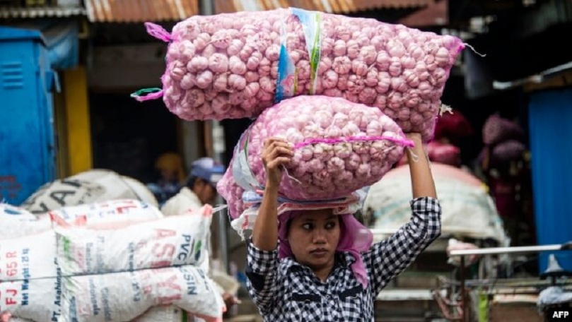 USUNG: Seorang perempuan menyunggi bawang putih di sebuah pasar tradisional di Surabaya.
