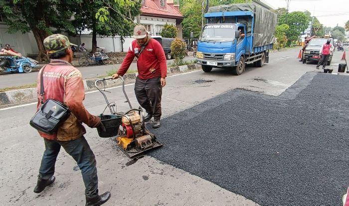 PERAWATAN JALAN: Petugas DSDABM Kota Surabaya melakukan penambalan di kawasan Jalan Pahlawan untuk memberikan keamanan dan kenyamanan bagi para pengendara, khususnya roda dua.