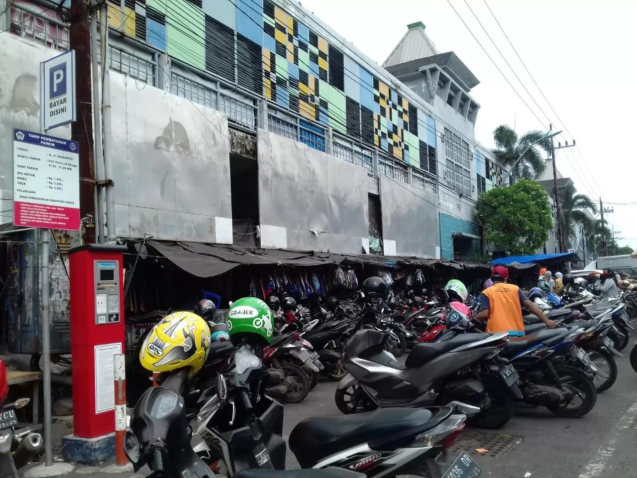 Suasana deretan kendaraan bermotor yang terparkir di pinggir jalan dengan pengawasan juru parkir.