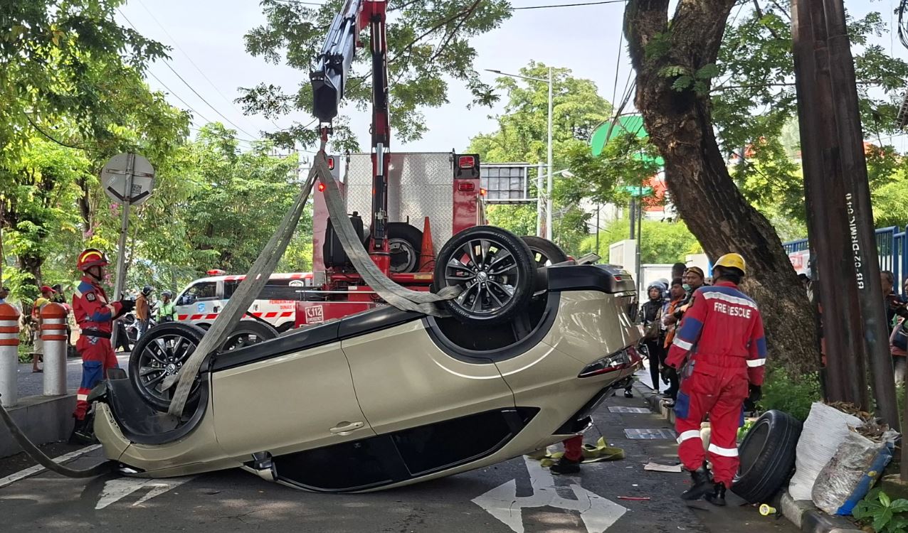 EVAKUASI: Mobil HR-V yang dikemudikan Dhemas Arya P (25), warga Babatan Wiyung, terbalik dan timpa motor setelah menabrak pembatas.