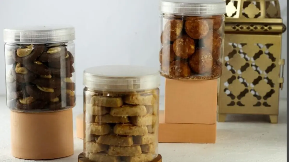 Tiga toples plastik berisi berbagai jenis kue kering yang ditata secara estetik di atas dekorasi minimalis.