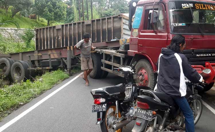 Kondisi truk kontainer yang tak kuat nanjak dan roda belakangnya nyemplung parit serta muatan kontainernya terguling. (Rizal Syatori/ Radar Pasuruan)