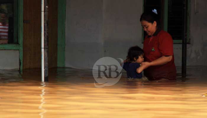 Seorang Ibu memapah anaknya melintasi banjir yang mengepung rumahnya di Dusun Kebrukan, Kedawung Kulon, Grati, Kabupaten Pasuruan. (Mokhamad Zubaidillah/ Radar Bromo)