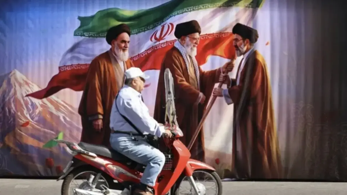Seorang pria mengendarai skuter melewati papan reklame yang menampilkan gambar mendiang pendiri Revolusi Islam dan Pemimpin Tertinggi Iran (Al-Jazeera)