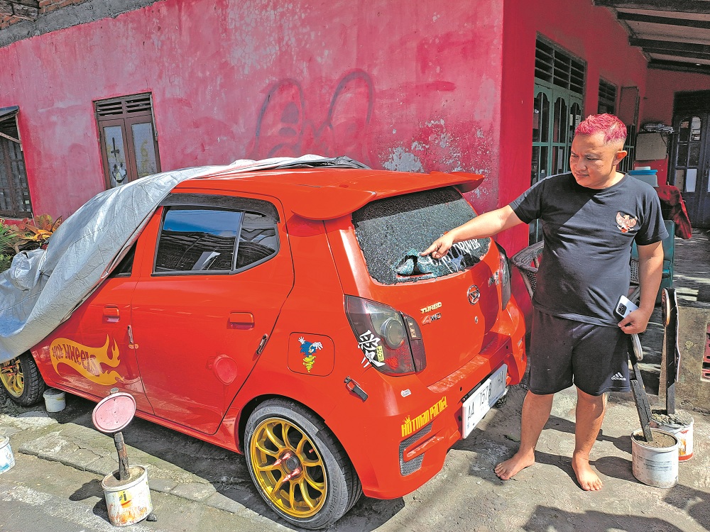 Zakaria menunjukkan kaca mobil yang dirusak sekelompok remaja bersenjata tajam, Minggu (14/1) dini hari.