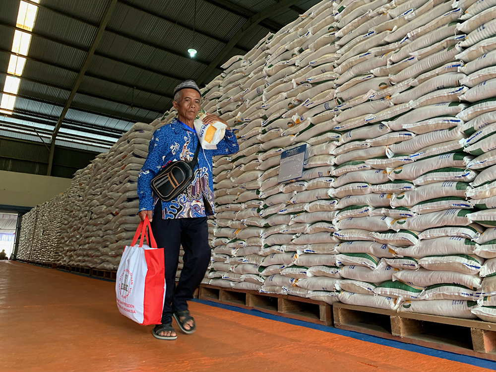 Warga melintas di antara tumpukan beras cadangan pangan di gudang Bulog Bengkal, Temanggung.
