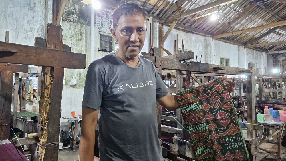 Umar Saleh berada di pabriknya dan menunjukkan hasil sarung tenun Botol Terbang buatannya.